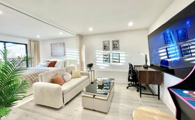 Open-plan living room with dining table, white sofa, wall-mounted TV, hardwood floors, and glass doors opening to patio